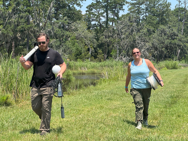 Students walking with equipment in the marsh