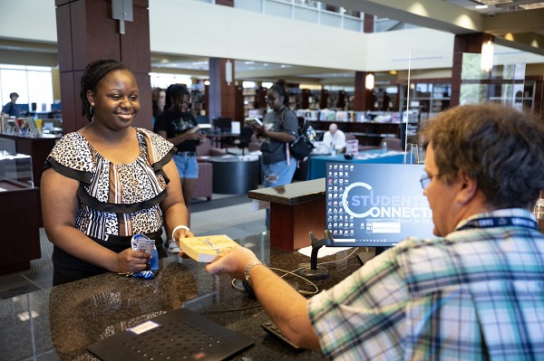 Student Being Handed Book at Library Desk