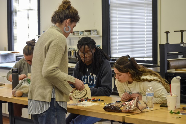 artist is teaching three students through hands on learning on an emboridory hoop
