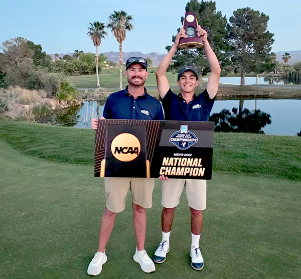 Two men holding trophies on golf course